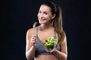 beautiful young woman eating salad over black background.