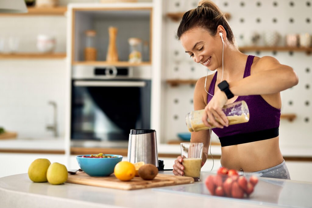 happy sportswoman pouring fruit smoothie in a glass in the kitch